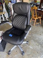 Black executive office chair with diamond-stitched upholstery, padded armrests, and caster wheels.