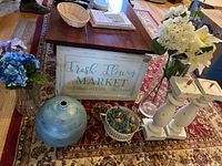 Overview of shabby chic decor assortment on a wooden coffee table including flowers, vases, sign, candle holders, and potpourri holder.