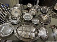 Photo showing collection of silver plated dishes, bowls, and trays arranged on surface