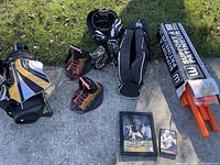 Photo of youth sports equipment including black, gold, and white golf bag, red and black baseball cleats and gloves, wakeboard bindings, and signed pictures.