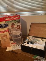 Honeywell Platinum Air Purifier in original box next to Tasco microscope case on a wooden floor near window blinds