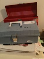 Closed gray and red toolboxes stacked on top of artist paper and a paint book, showing overall lot contents.