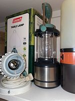 Photo showing Coleman table lamp in box, camping lantern, and plastic bucket with lid