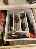 Cutlery tray with stainless steel forks, knives, spoons, and a large serrated knife with orange safety cap