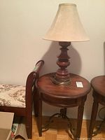 Round wooden end table with metal scrollwork base and lamp on top, showing full height and table size.