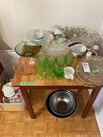 Photo showing the assembled set of glassware, serving bowls, dessert bowls, and two steel bowls on a wooden table with a parquet floor.