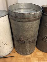 Full view of the metal grain bin showing the body and lid with a ring handle on the side