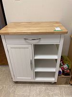 Front view of the kitchen cart showing wood top, drawer, cabinet door, and open shelves.