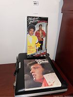 Michael Jackson doll in original box standing on music briefcase with Elvis book on top