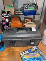 Photo of the Ronco Flower Loom box, knitting needles, two bead holders, and toolboxes arranged on a wooden floor.