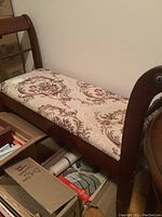 Side angle view of the upholstered bench showing the floral seat cushion and dark wood armrest with brass-like accent.
