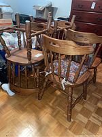 Six ash wood spindle back dining chairs, some stacked, showing overall condition and chair design including legs and seat cushions.