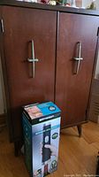 Front view of the bar cabinet showing wooden doors with metal handles and box of electric wine opener in front.