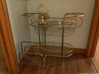 Brass serving cart with glass shelves, touch lamp on top, and magazine rack placed beside cart