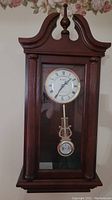 Front view of Bulova wooden wall clock with glass door showing clock face and pendulum.