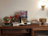 Wide view showing all lot items on wooden surface including globe, flowers, clock, barometer, vase, plates, and bowl.