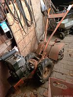 Side view of cultivator showing wheels, tines and engine mounted on steel frame