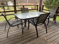 Outdoor rectangular glass top table surrounded by four metal framed stacking sling chairs on a wooden deck.