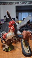 Photo showing all three figurines (horse, rooster, eagle) on a wooden surface with visible detail and damage.
