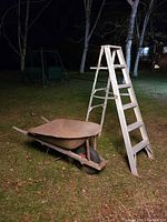 Aluminum folding step ladder and metal wheelbarrow outdoors on grass at night, showing overall condition.