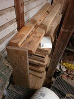 Stack of mixed lumber remnants including broad 4x4 pieces and thinner 2x4 pieces against shed wall.