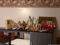 Overview of religious collection showing statues, crucifixes, Bible, prints, and rosary beads on black shelf