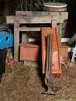 Wooden saw horses with metal holders, orange metal ramps behind and a farm-grade jack in front, all placed outdoors on the ground.