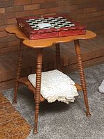 Overall view of the spindle leg side table with the chessboard and doilies visible on and under it.