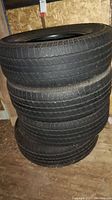 Stack of four Goodyear tires, size 265/70/R17, shown in small wooden shed with visible tread and sidewall details.