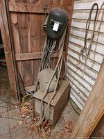 Dusty Canox arc welding unit stacked with two black welding masks and cables in a shed corner.