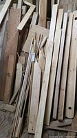 Stack of assorted wood planks, boards, and dowels leaning against a wall.