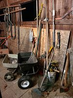 Wide angled photo showing the yard tools including spreaders, rakes, and axes arranged against a wall in a shed.