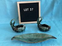 Two Blue Mountain Pottery swans and one long leaf-shaped dish arranged on a blue backdrop with a sign reading 'LOT 37'.