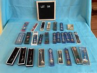 Lot of 22 boxed collectible spoons arranged in rows on blue backdrop with lot number sign behind.