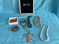 Full lot photo showing all jewelry laid out on blue fabric background including multiple necklaces, bracelets, amber glass beads, and pendant earring set.
