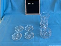 Four crystal coasters displayed next to crystal vase and small bowl on blue background, showing front view of items