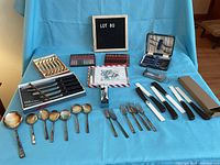 Wide view of assorted cutlery on blue backdrop showing various sets of spoons, forks, and knives