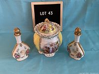 Photo showing lidded candy dish and two matching cordial bottles with floral and classical designs