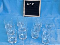 Photo of two sets of tumblers arranged on blue cloth, smaller faceted crystal tumblers on right and larger clear glass tumblers on left