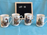 Photo showing four white ceramic mugs with gold rim, each featuring a unique Norman Rockwell artwork reproduction showing people in nostalgic scenes.