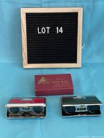 Two sets of pop-up opera glasses (red and black) with original box placed on blue cloth background
