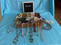 Wide shot of assorted vintage costume beaded necklaces laid out on a wooden box and blue fabric background.
