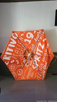 Patio umbrella opened showing Aperol Spritz branding and one corner tear.