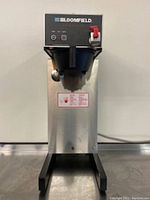 Front view of Bloomfield E.B.C coffee brewer showing control panel with buttons and red faucet.