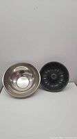 Photo showing one 12 inch stainless steel mixing bowl and one 10 inch black metal bundt cake pan side by side on a white surface against a white wall.