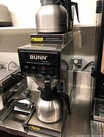 Front angled view of BUNN coffee brewer with stainless steel coffee pot on lower warmer.