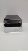 Front angle photo of vintage metal napkin dispenser showing the shiny chrome face with black napkin dispensing slot.