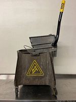 Front angled view of the commercial mop bucket with wringer and caution sign on the side.
