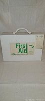 Closed white metal first aid box with first aid label and a list on the front right side.