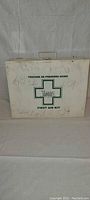 White metal box labeled as a first aid kit, showing exterior condition and markings